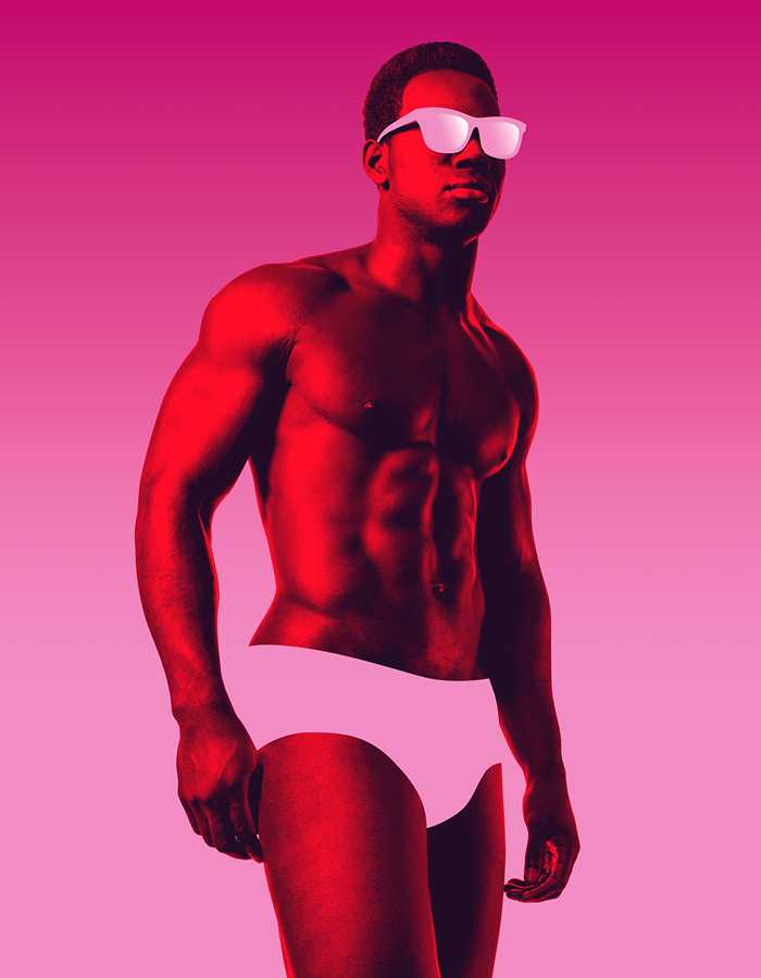A Black man wearing sunglasses and underwear stands in front of a bright pink background.