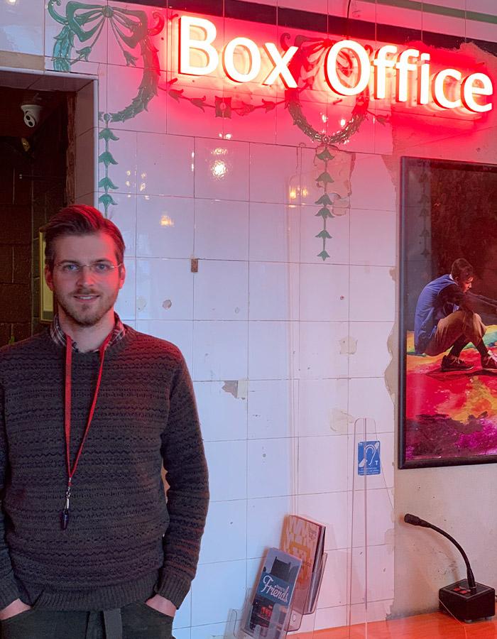 A man standing in front of a LED neon light saying Box Office