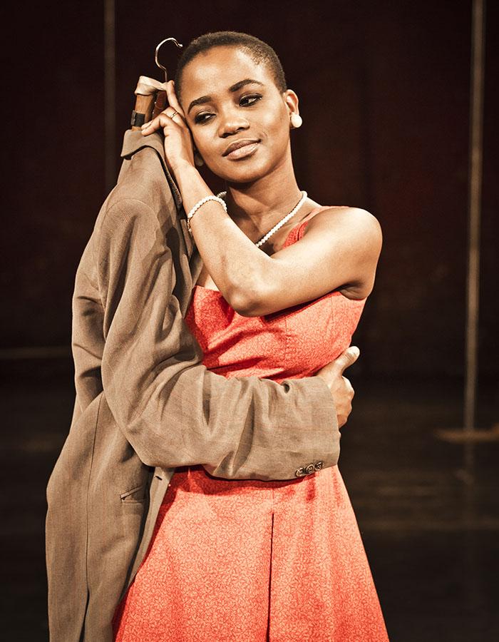 A woman in an orange dress hugs a suit that is being worn by an invisible person with only their hand showing