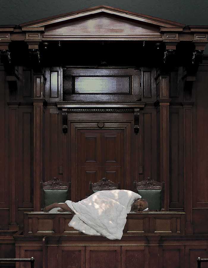 An elderly man lies on a table in the House of Commons wrapped in a white blanket.