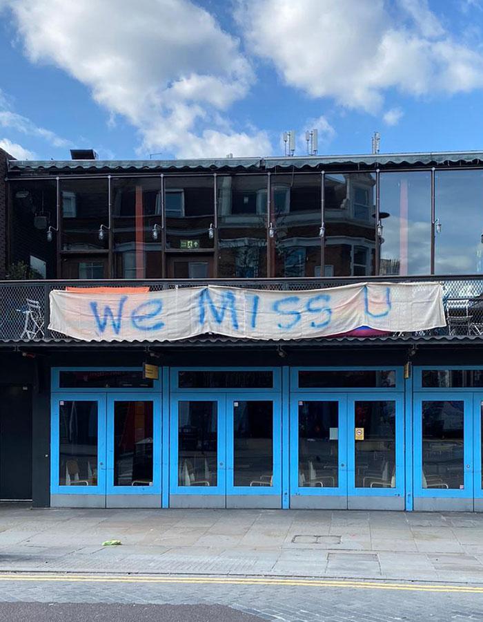 A banner with the words 'We Miss You' hangs outside the Young Vic theatre