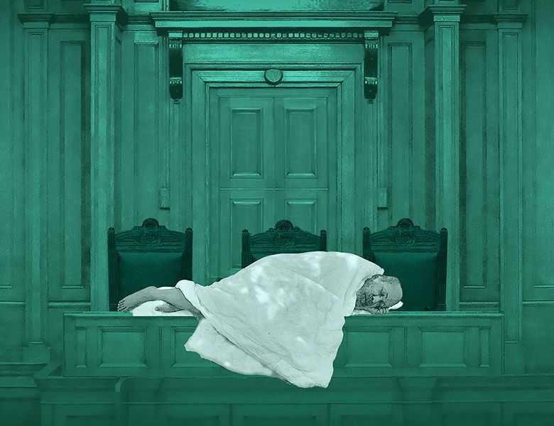Against a teal background, an elderly man lies on a table in the House of Commons wrapped in a white blanket. 