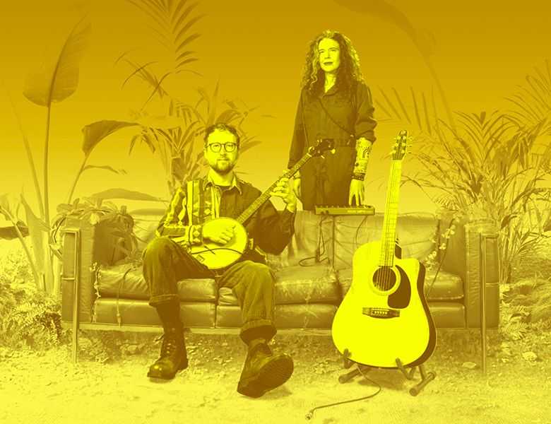 Against a yellow background are a man and woman. The man sits on a sofa and is holding a banjo; the woman stands behind the sofa. Next to them is a guitar on a stand. 
