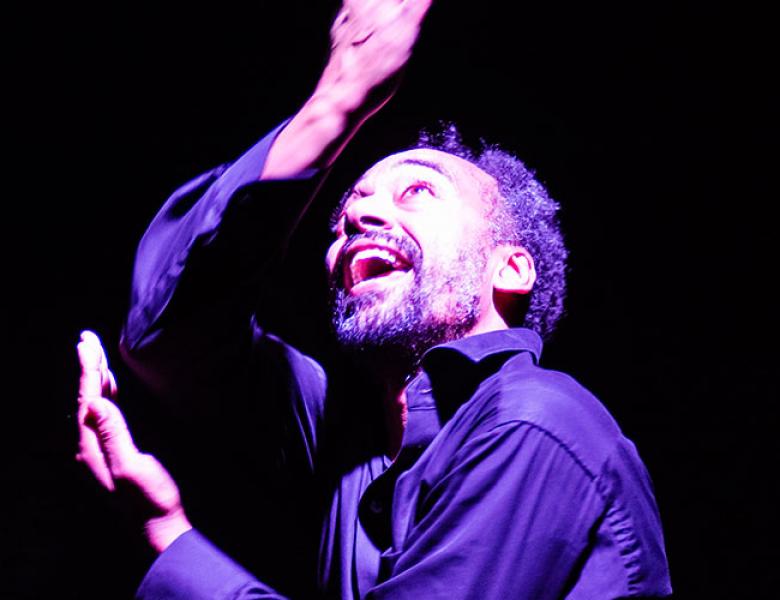 Man in a darkly lit atmosphere, arms stretched, looking upwards 