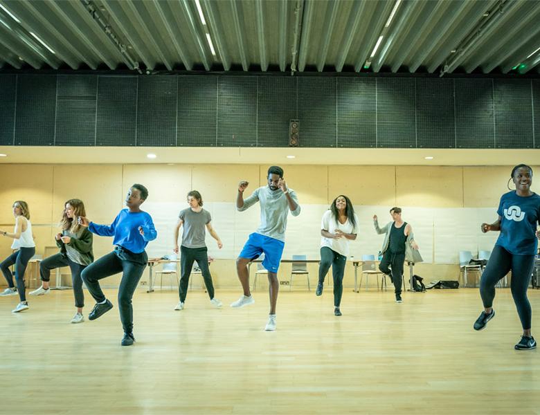 The company of Fairview dancing in a row in the rehearsal room