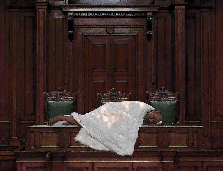 An elderly man lies on a table in the House of Commons wrapped in a white blanket. 