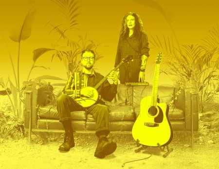 Against a yellow background are a man and woman. The man sits on a sofa and is holding a banjo; the woman stands behind the sofa. Next to them is a guitar on a stand. 