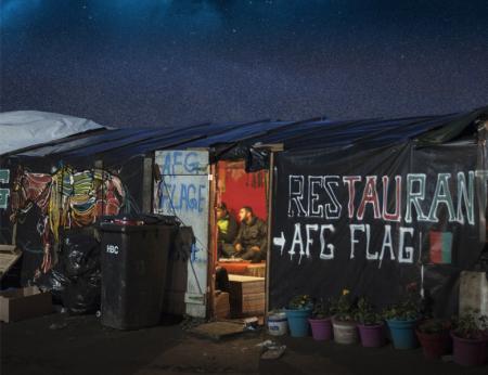 External photo looking into the dimly lit doorway of the temporary structure known as the Afghan Cafe in the Calais 'jungle' taken by  Giulio Piscitell