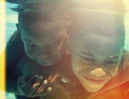 Two young boys under the water smiling, holding each other tightly