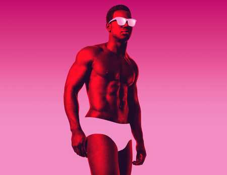 A Black man wearing sunglasses and underwear stands in front of a bright pink background. 