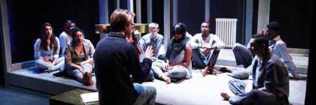 Man talking to a group of young people as they all sit on the stage