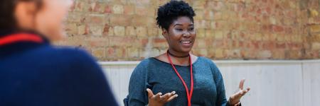 A Young Vic Young Associate sits smiling, open armed in a workshop looking across the room