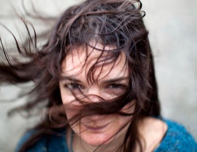 brunette women in a blue top with the wind blowing in here face that half of her face is covered.