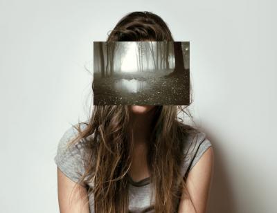 Female in front of a plain grey backdrop with her face concealed by an image of a misty forest