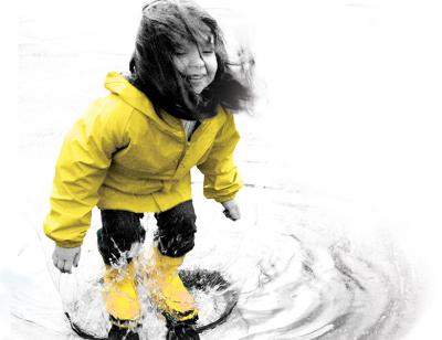 Little girl in a yellow jacket plays in a puddle