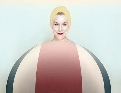 A smiling Juliet Stevenson is superimposed coming out the top of a striped oversized red, white and blue beach ball, almost as if the ball was her body.
