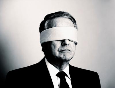 A man in a suite, with black tie, blindfolded 