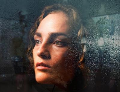 Woman looks pensively out window covered in rain drops 