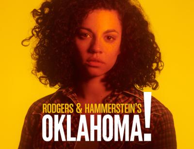 Rodger's & Hammerstein's Oklahoma! From 27th April to 25th June. Image description: A woman with curly hair, wearing a checked shirt, bathed in orange light in front of a yellow background